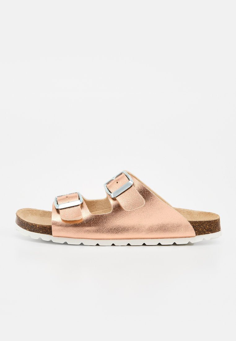 Offener Slide-Sandalette mit zwei verstellbaren, roségoldenen Metallic-Riemen, Kork-Fußbett und weißer, strukturierter Sohle, in Seitenansicht gezeigt.