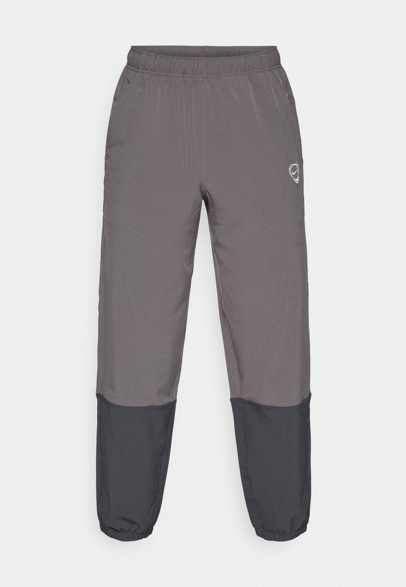 Graue Sporthose mit elastischem Bund, zwei Seitentaschen und schwarzen unteren Einsätzen. Hergestellt aus einem leichten Material, mit einem Logo-Detail.