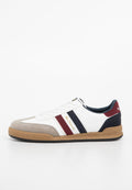 Weißer Sneaker mit grauem Wildleder-Zehenteil, blauen und roten gestreiften Akzenten und tanfarbener Gummisohle. Verfügt über ein Schnürdesign und ein goldenes Logo an der Seite.