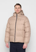 Mann trägt beige Steppjacke mit Kapuze und Frontreißverschluss, steht vor hellem einfarbigem Hintergrund.