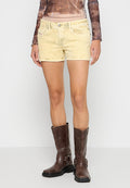 Gelbe Jeansshorts mit einem ausgewaschenen Look, fünf Taschen und kontrastierenden Nähten, kombiniert mit braunen Leder-Motorradstiefeln.
