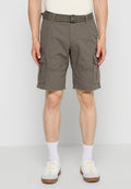 Mann trägt braune Cargoshorts mit Seitentaschen, weiße Socken und weiße Sneakers, steht vor einem schlichten hellgrauen Hintergrund.