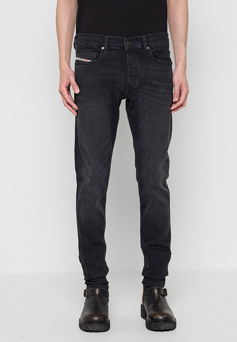 Schwarze Slim-Fit-Jeans mit fünf Taschen, Knopf- und Reißverschluss sowie dezenter Textur. Kombiniert mit dunklen Lederstiefeln.