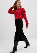 Rote Bluse mit schwarzem Spritzer-Muster und Rüschenschößen, kombiniert mit einem schwarzen Satin-Maxirock und knielangen schwarzen Stiefeln.