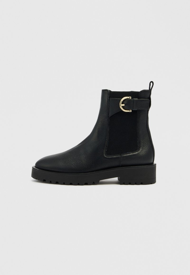 Schwarze Stiefeletten aus strukturiertem Leder mit gerippten elastischen Seitenteilen, einem runden goldfarbenen Akzent und einer dicken, robusten Sohle.