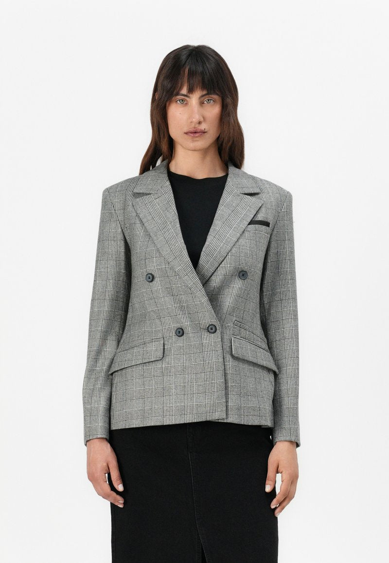 Doppelt gefütterter Blazer im grauen Hahnentpattern, mit Spitzenlapels, zwei Fronttaschen und Knopfakzenten, kombiniert mit einem schwarzen Oberteil.