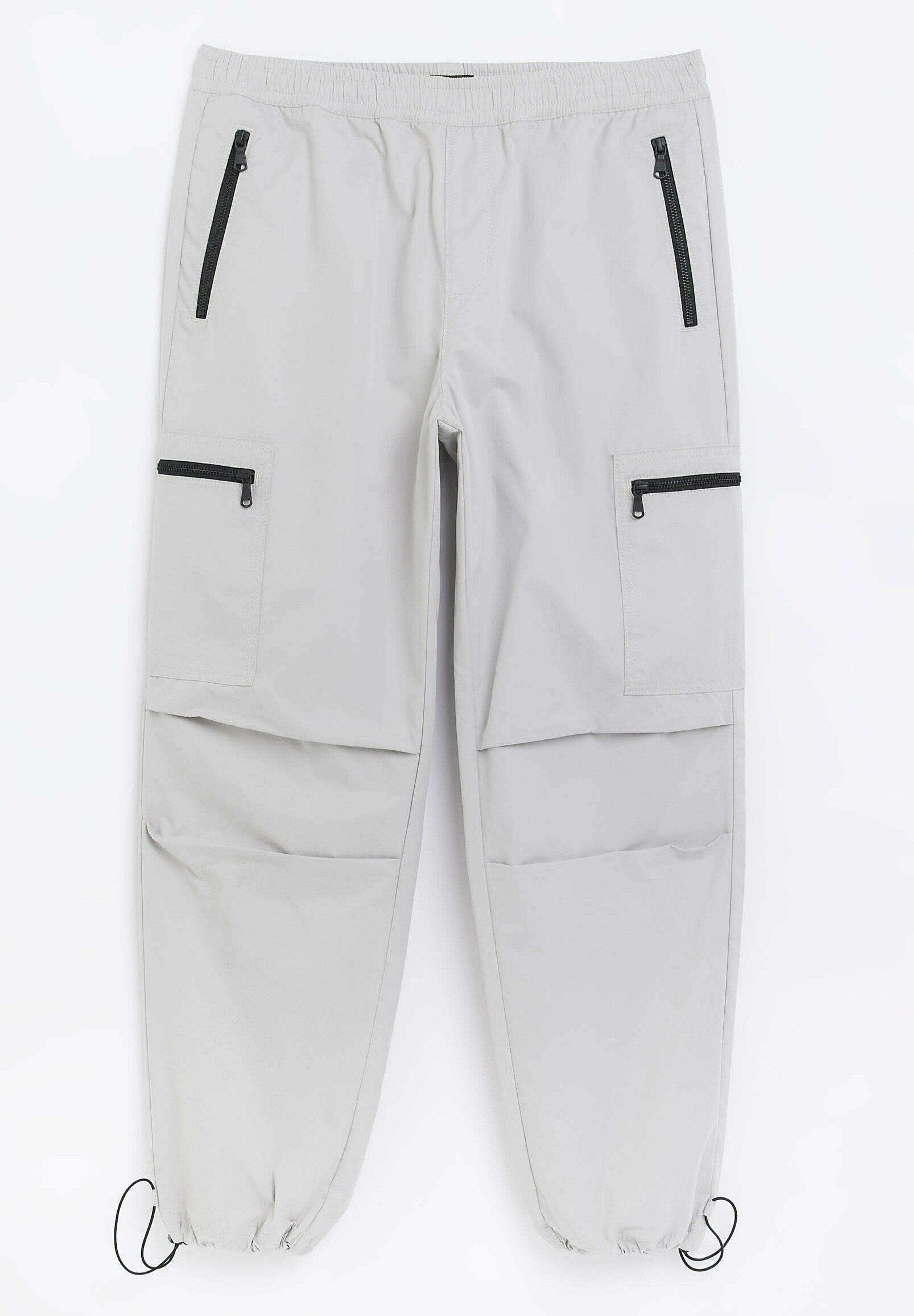 Hellgraue Cargo-Hose mit elastischem Bund, Reißverschluss vorne und seitlichen Taschen sowie verstellbaren Säumen. Glattes, synthetisches Material mit minimalen Falten.
