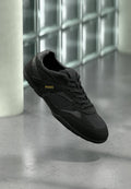 Schwarzer Sportschuh mit dem "HUGO"-Logo in Gold an der Seite, schwarzen Schnürsenkeln und strukturierten Einsätzen, schwebend über einem polierten Betonboden.
