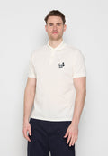 Mann mit kurzen braunen Haaren, der ein weißes kurzärmeliges Poloshirt mit einem kleinen schwarzen Logo auf der Brust und dunkle Hosen trägt, steht vor einem einfarbigen Hintergrund.