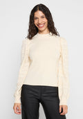 Cremesweater mit geripptem Körper und Puffärmeln im Spitzenmuster. Verfügt über einen hohen Kragen und enganliegende Bündchen, kombiniert mit schwarzen Hosen.