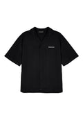 Schwarzes kurzärmliges Shirt mit lockerer Passform, Knopfverschluss und weißem "PEGADOR"-Logo auf der linken Brustseite. Glatte Stofftextur.