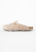 Beige Wildlederclogs mit runder Form, einem kleinen kreisförmigen Ausschnitt und einem Kork-Akzent am Absatz. Durchsichtige, strukturierte Sohle mit einem gesprenkelten Muster.