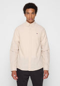 Langärmliges Hemd mit Knopfleiste aus hellem Beige, mit Kragen, vorderen Knöpfen und einem kleinen Logo auf der Brust.