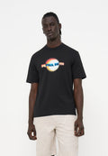 Mann trägt schwarzes T-Shirt mit buntem, unscharfem "PS Paul Smith"-Logo und hell strukturierten Shorts, steht vor einfarbig weißem Hintergrund.