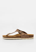 Braune Wildleder-Flip-Flops mit verstellbarer Schnalle, Kork-Fußbett und weißer Gummisohle, Seitenansicht auf einfarbigem Hintergrund.