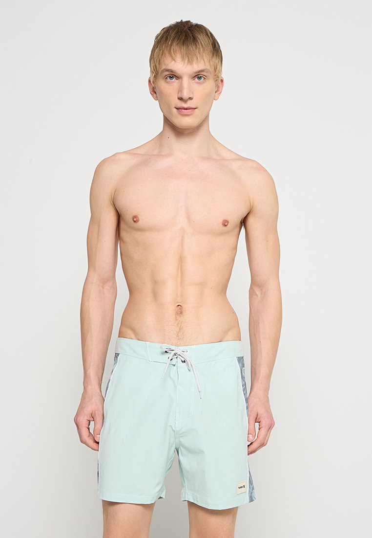 Hellblaue Badeshorts mit einem Kordelzugbund, seitlichen Einsätzen in einem dunklen Muster und einem kleinen Markenlogo an der unteren Seite.