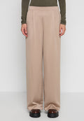 Beige Hosen mit weitem Bein und einer glatten, weichen Textur, ausgestattet mit vorderen Falten und einem Taillenbund. Kombiniert mit klobigen schwarzen Plateauschuhen.