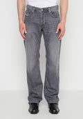 Mann trägt ausgewaschene graue Jeans mit geradem Bein, weißes Hemd eingesteckt und schwarze Lederschuhe, steht vor einem schlichten Hintergrund.