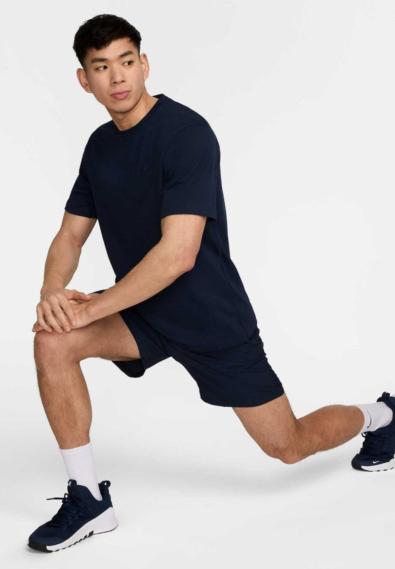 Navyblaues Sport-T-Shirt und Shorts aus leichtem Material. Das Modell befindet sich in einer Ausfallschritt-Position, trägt weiße Socken und navyblaue Schuhe mit weißen Akzenten.