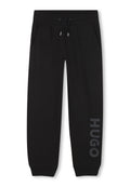 Schwarze Sweatpants aus weichem Material, mit seitlichen Taschen, einem Kordelzugbund und "HUGO" in Grau entlang des linken Beins aufgedruckt.