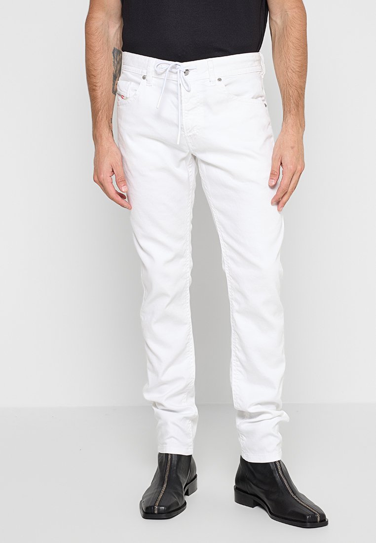 Weiße Jeans mit geradem Schnitt, ausgestattet mit Fronttaschen, Gürtelschlaufen und einem Kordelzug an der Taille. Kombiniert mit schwarzen Reißverschlussstiefeln.