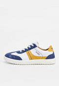 Weißer Sneaker mit blauen und gelben Wildlederakzenten, weißen Schnürsenkeln und der Aufschrift "1893" an der Seite und der Sohle.