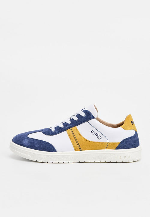 Weißer Sneaker mit blauen und gelben Wildlederakzenten, weißen Schnürsenkeln und der Aufschrift "1893" an der Seite und der Sohle.
