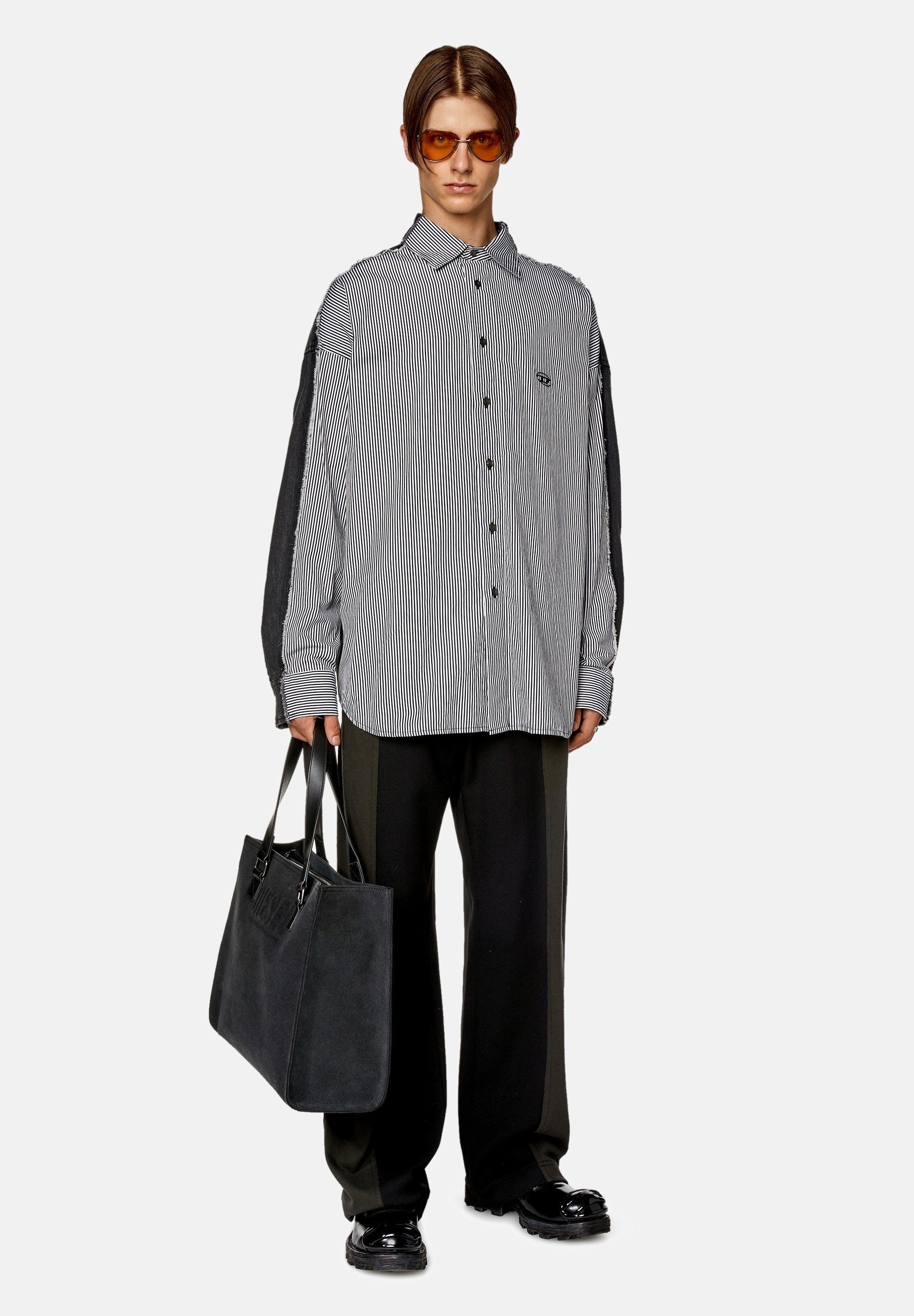 Gestreifte Button-Down-Bluse mit langen grauen Ärmeln, schwarze Hose und eine große schwarze Tragetasche. Das Model trägt braune Sonnenbrillen.
