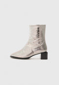 Metallisch silberner Knöchelstiefel mit spitzer Zehe und Blockabsatz. Glatte Textur, elegantes Design und minimalistische Nähdetails.