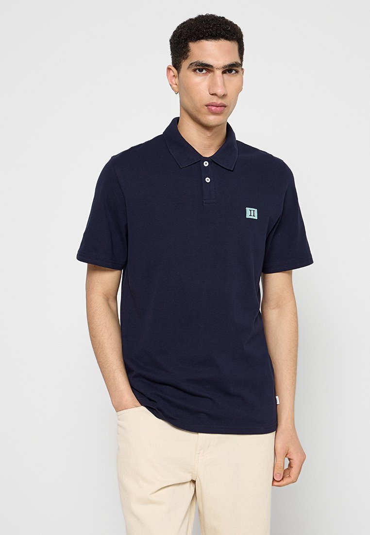 Dunkelblaues Polohemd aus Baumwolle, mit Kragen, drei Knöpfen und einem gestickten hellblauen Logo auf der linken Brust.