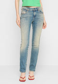 Frau in ausgewaschenen blauen Skinny-Jeans, grünem cropped Top und roten Flip-Flops, die vor einem schlichten hellen Hintergrund steht.