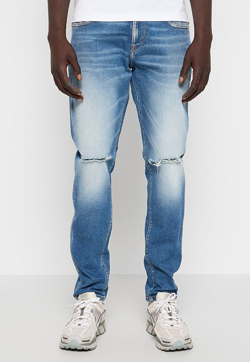 Hellblaue Denim-Jeans mit schmaler Passform, ausgewaschenem Look und verwaschenen Knie-Details. Kombiniert mit beigen Sneakern.