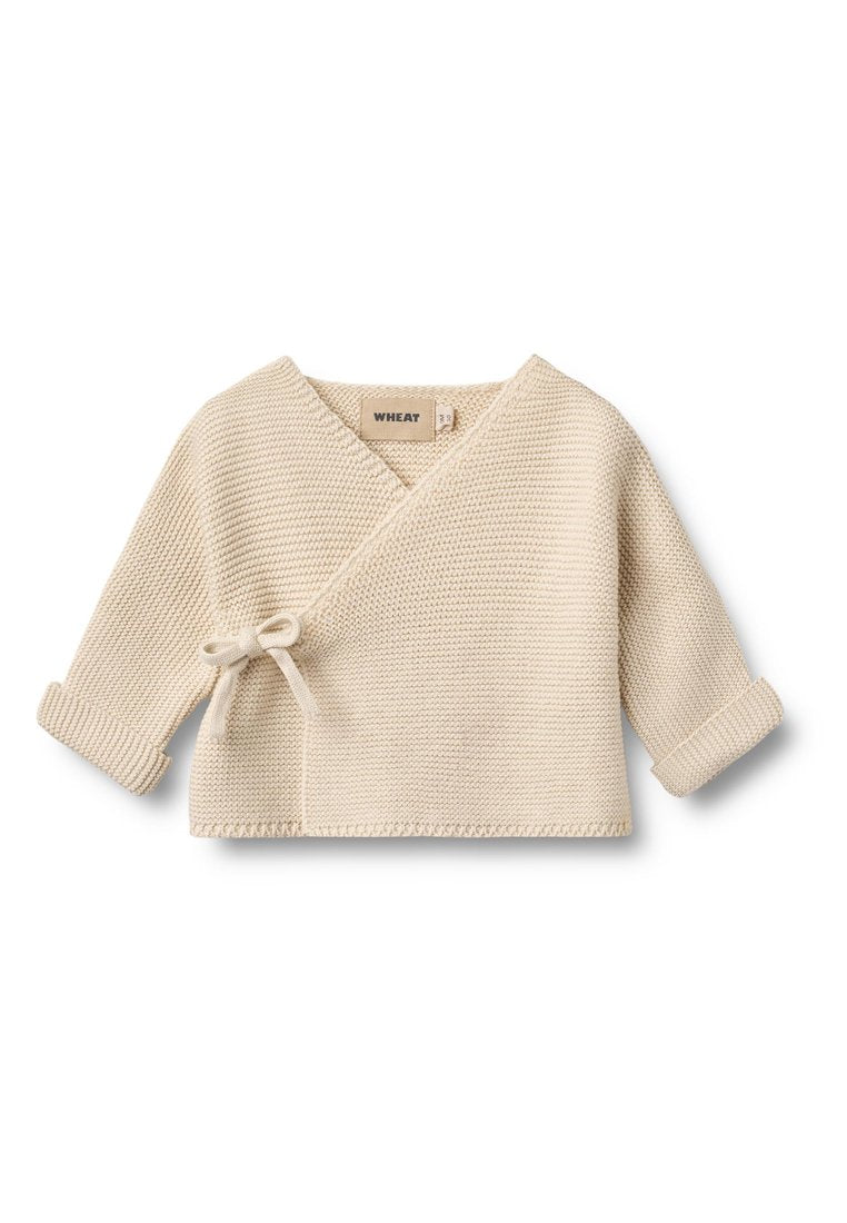 Cremefarbener, gestrickter Wickelpullover mit V-Ausschnitt, seitlicher Bindung und hochgekrempelten Ärmeln. Hergestellt aus weichem, strukturiertem Stoff.