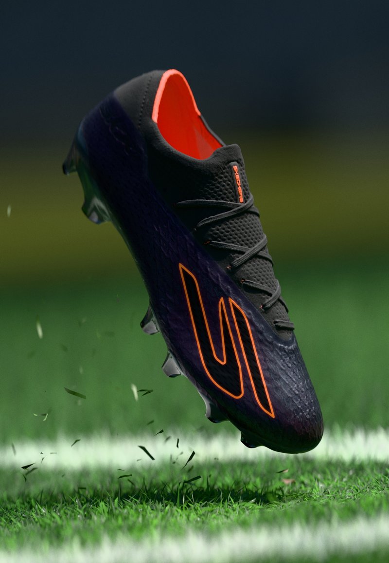 Schwarzer Fußballschuh mit orangefarbenem Innenfutter und Logo, strukturiertem Obermaterial und geformter Stollen-Sohle, in der Luft über grünem Gras aufgenommen.