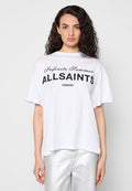 Frau mit lockigem Haar, die ein weißes AllSaints "Infinite Summer" T-Shirt und silberne Hosen trägt, steht vor einem schlichten hellen Hintergrund.