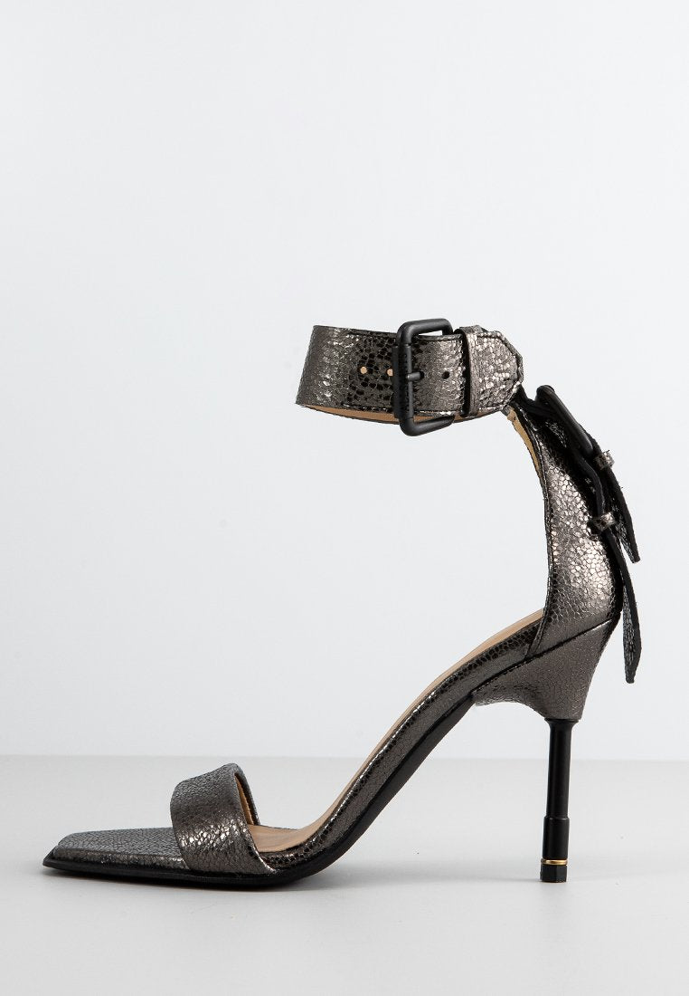 Metallisch graue High-Heel-Sandalette mit Knöchelriemen, quadratischer Zehenpartie, strukturiertem Finish und schwarzem Stiletto-Absatz. Schnallendetail am Riemen.