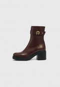 Dunkelbrauner Leder-Stiefelette mit Blockabsatz, schwarzer Sohle und dekorativem Riemen mit goldener Schnalle auf weißem Hintergrund.