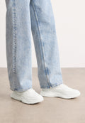 Weiße Sportsneaker mit einem glatten, geformten Design und strukturierten Sohlen, kombiniert mit hellblauen, locker sitzenden Jeans.