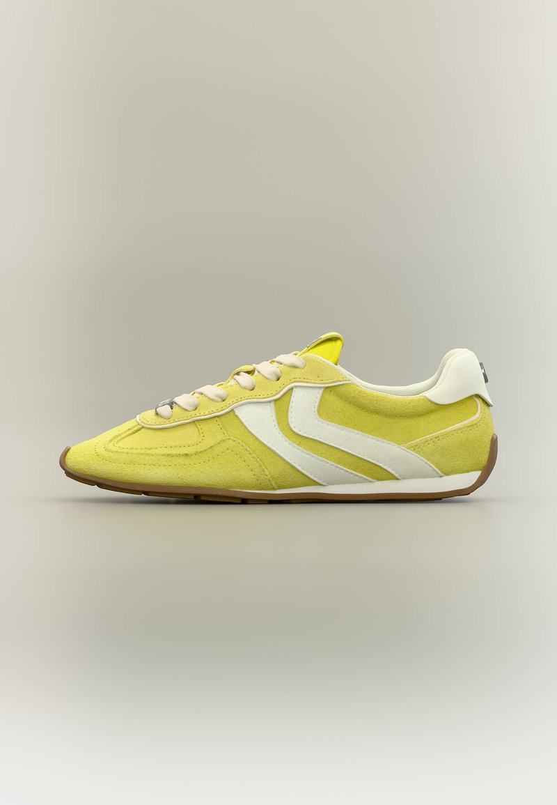 Gelber Wildledersneaker mit weißen Seitenstreifen, weißen Schnürsenkeln und brauner Gummisohle, von der rechten Seite auf neutralem Hintergrund gezeigt.
