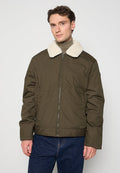 Olivgrüne Jacke mit einem weichen, weißen Kunstpelzkragen, Reißverschluss und Seitentaschen. Das Material wirkt glatt mit matter Oberfläche.