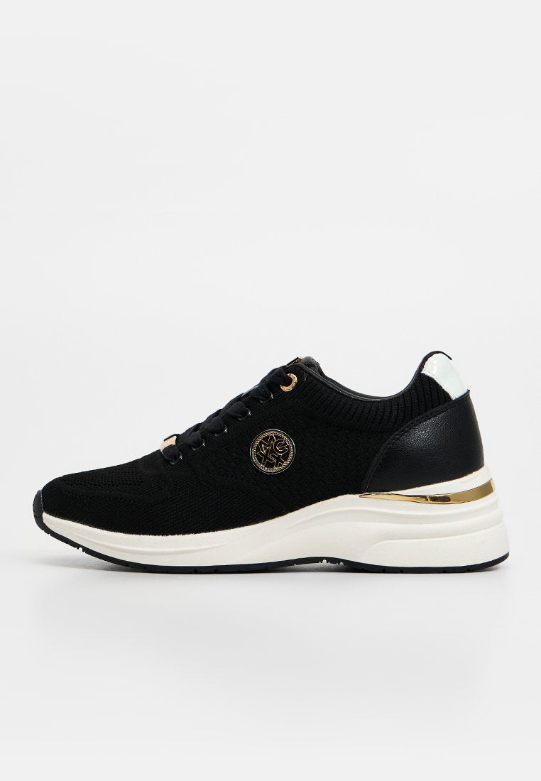 Schwarzer Strick-Sneaker mit weißer Sohle, goldenen Akzenten, Schnürverschluss vorne und rundem goldfarbenem Emblem an der Seite, in rechter Seitenansicht gezeigt.