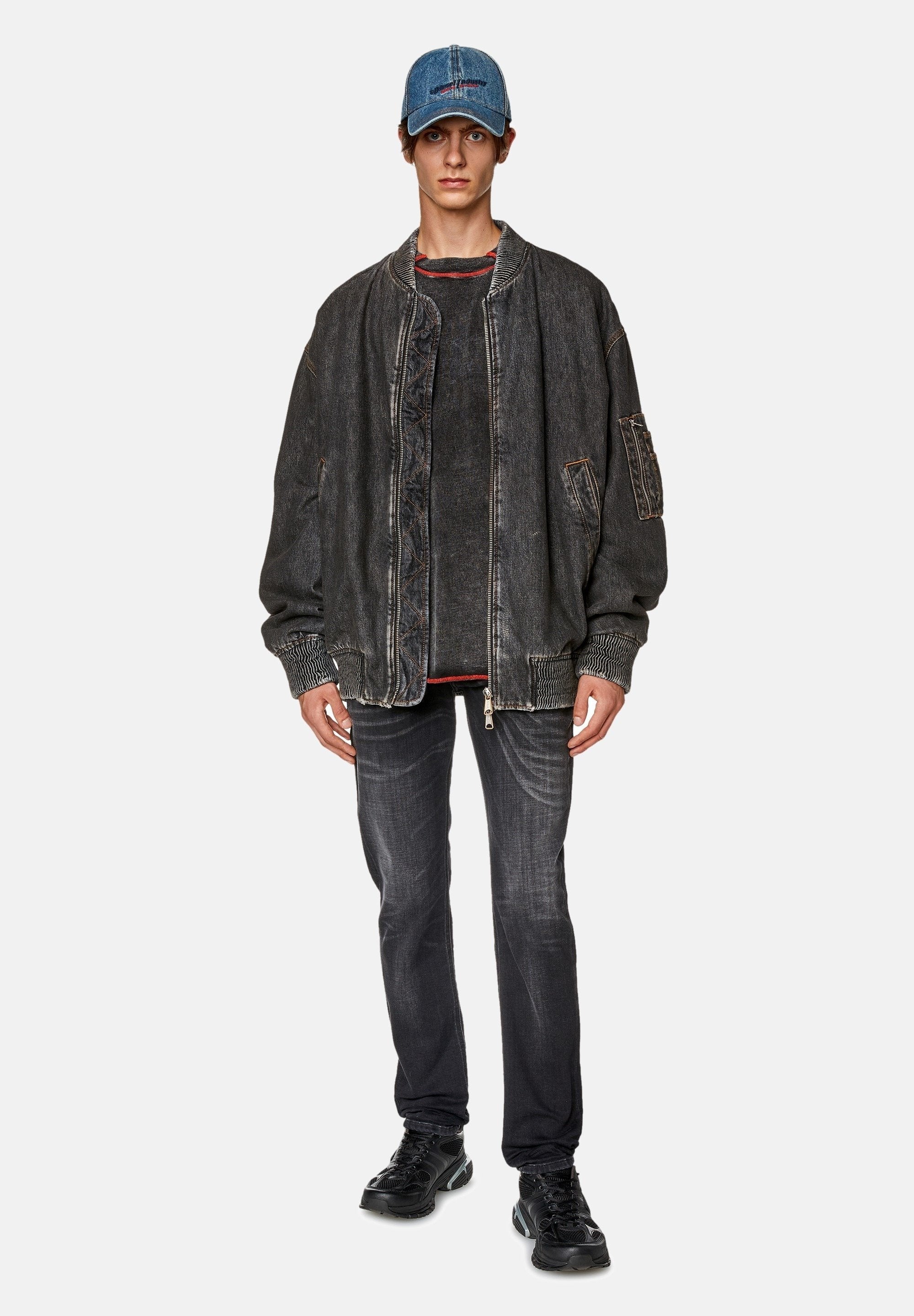Schwarze Jeans-Bomberjacke mit gerippten Bündchen, kombiniert mit einem dunklen Langarmshirt, Jeans und einer hellblauen Jeansmütze. Schwarze Turnschuhe.