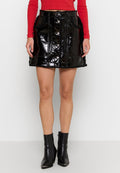 Frau in einem glänzenden schwarzen Minirock mit Knopfleiste und Taschen, kombiniert mit schwarzen Stiefeletten und einem roten, langärmligen Cropped-Top.