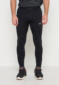 Mann trägt schwarze enganliegende Sportleggings und schwarze Sportschuhe mit roten Details und steht vor einem schlichten weißen Hintergrund.