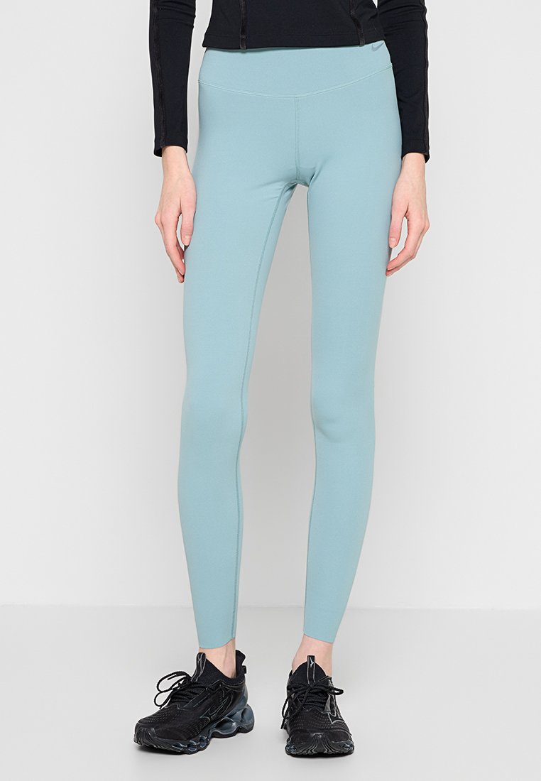 Hellblaue Leggings aus dehnbarem Stoff mit hoher Taille und figurbetonter Silhouette, kombiniert mit schwarzen Sportschuhen.