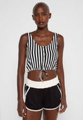 Frau in einem ärmellosen Crop-Top mit schwarzen und weißen vertikalen Streifen und Knöpfen sowie schwarzen Sportshorts mit weißem Saum.