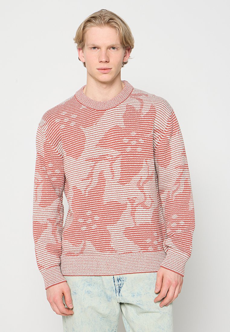 Rot-weiß gestreifter Strickpullover mit Rundhalsausschnitt, einem gemusterten Design und gerippten Bündchen an Ärmeln und Saum, kombiniert mit hellblauen Jeans aus Denim.