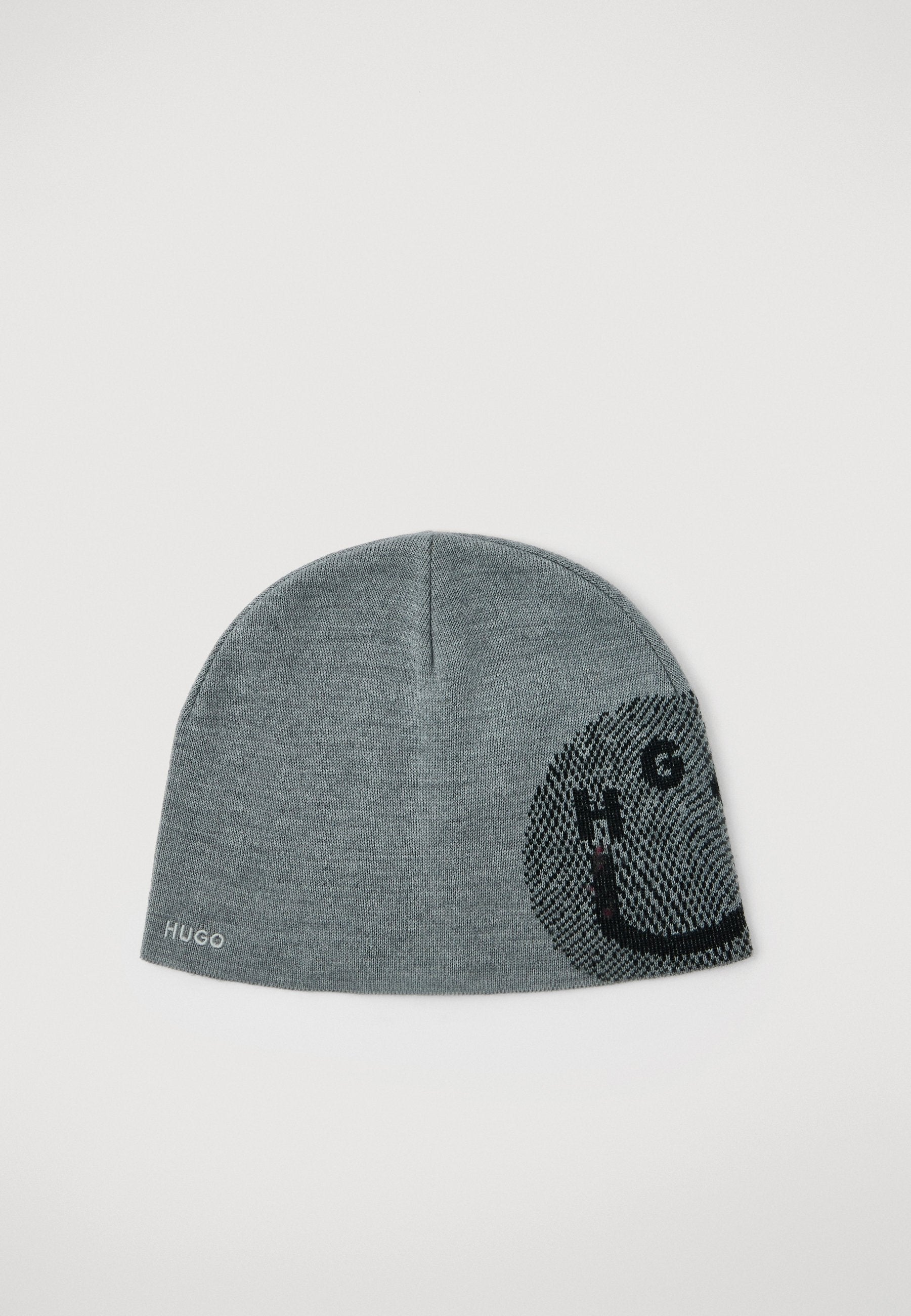 Graue Strickmütze mit einem schwarzen und dunkelgrauen Smiley-Gesichtsmuster auf einer Seite und dem Text "HUGO" in der Nähe des Randes.