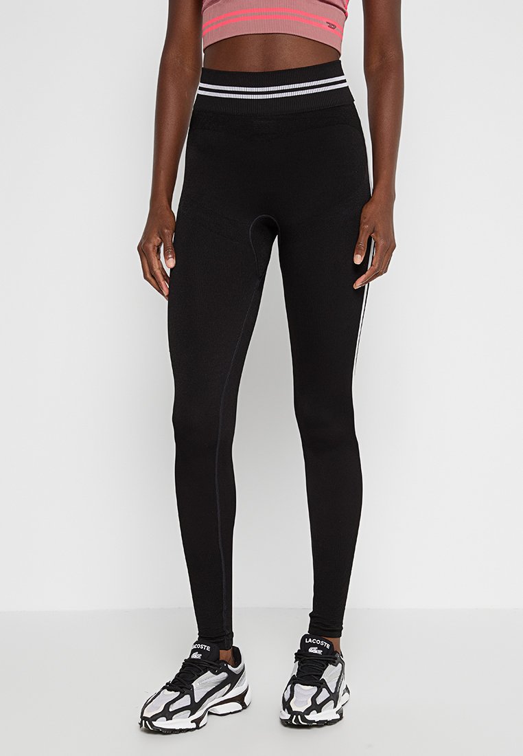 Schwarze Leggings mit figurbetontem Schnitt, ausgestattet mit einem hohen Bund und dünnen weißen seitlichen Streifen, hergestellt aus einem glatten, dehnbaren Stoff.