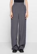 Graue weitgeschnittene Hosen mit glatter Textur, hoher Taille und minimalistischem Design. Sie zeichnen sich durch klare Linien und dezente Drapierung aus und werden mit schwarzen Schuhen kombiniert.